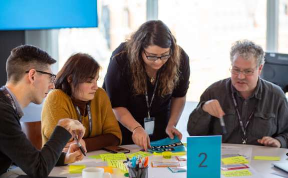 A group of academics sitting at a table working as part of a group. On the table there are pens, paper and notepads.